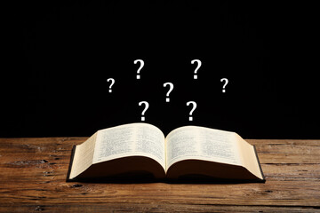 Question marks over open book on wooden table against black background