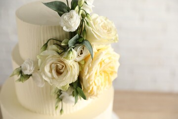 Delicious wedding cake decorated with flowers on blurred background, closeup