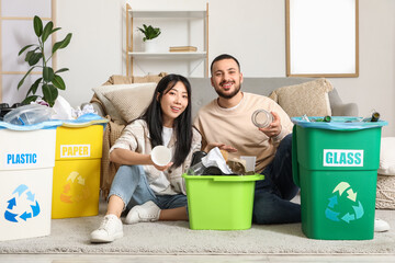 Young couple sorting rubbish in garbage bins at home. Global Recycling Day