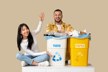 Young couple with sorted rubbish in garbage bins on beige background. Global Recycling Day
