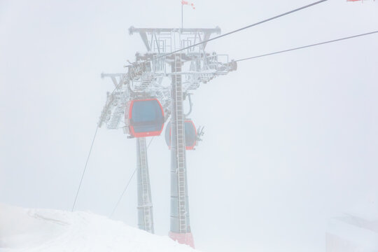 Red cable car against a snowy mountain backdrop in dense fog