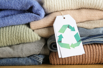Stacks of clothes and tag with recycling logo on table, closeup