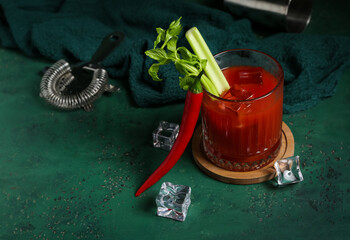 Glass of bloody mary cocktail with celery, chili pepper and ice cubes on green background