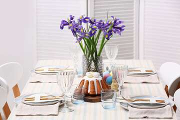 Table setting with Easter cake and flowers in room
