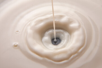 A close-up of milk splashing into a white liquid, creating ripples and a mesmerizing vortex....
