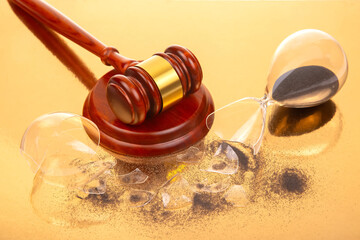 A finely crafted wooden gavel stands beside a fractured hourglass with black sand, photographed on...
