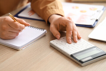 Female accountant with calculator and notebook at table in office