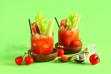 Glasses of bloody mary cocktail with bacon and celery on green background