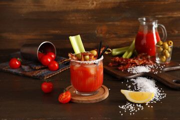 Glass of bloody mary cocktail with bacon, olives and celery on wooden background