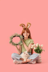 Cute girl with adorable cat, festive wreath and tulip flowers sitting on pink background. Easter celebration