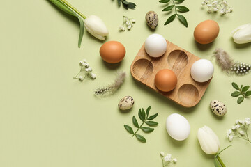 Composition with egg holder, Easter eggs, green leaves and feathers on green background