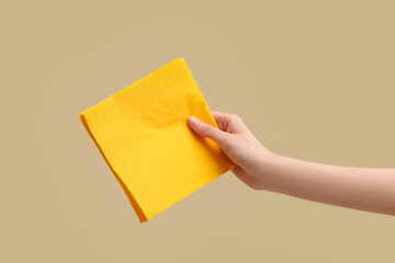 Female hand with yellow paper napkins on beige background