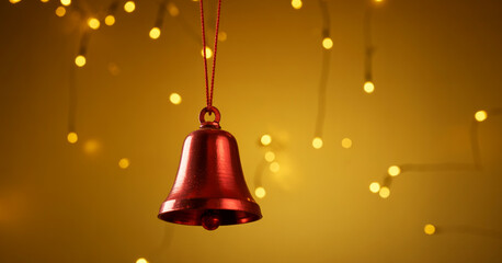 Obraz premium A close-up photograph of a red metal Christmas bell hanging against a golden bokeh background