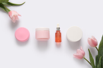 Different cosmetics and beautiful flowers on light background