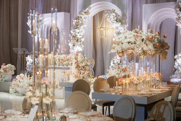 A luxurious wedding reception with rich floral decorations. Wedding banquet with a beautiful floral installation on white arches and candles in glass candle holders, creating a romantic atmosphere
