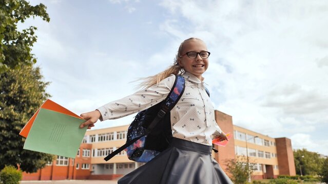 Schoolgirl running near campus, carrying notebooks, wearing backpack and glasses, embracing academic excitement