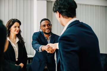 During a successful business partnership meeting, a cheerful young manager shakes hands with a new employee. Close-up of the handshake in the office, symbolizing teamwork and collaboration.