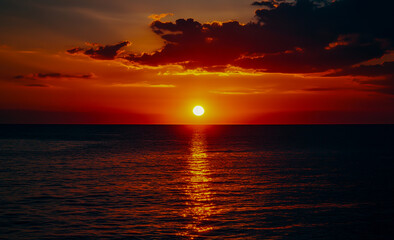 Obraz premium A calm and enchanting sunset over the sea, a vibrant orange sun sinking below the horizon, casting a warm glow over the calm sea.