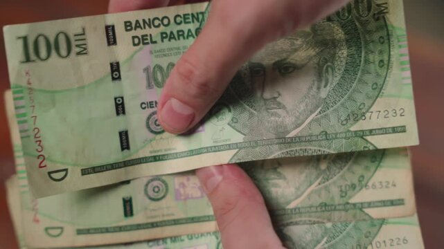 Fingers counting one-hundred-thousand guaran&iacute; bills from Paraguay