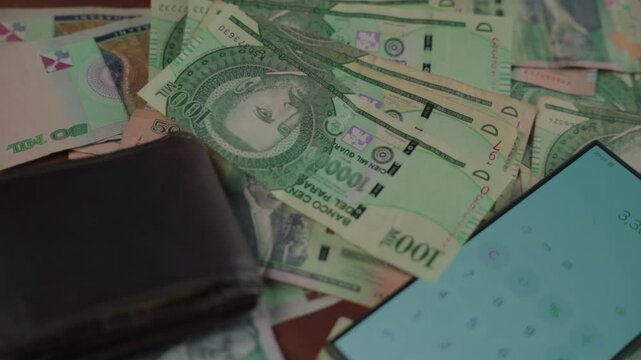 Panoramic close-up of Paraguayan currency bills with a cellphone and wallet