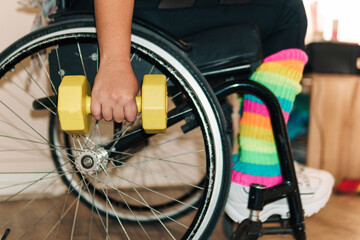 View of a woman in a wheelchair and her hands, exercising and carrying dumbbells, in a gym, view of a woman's hands with dumbbells in a wheelchair.