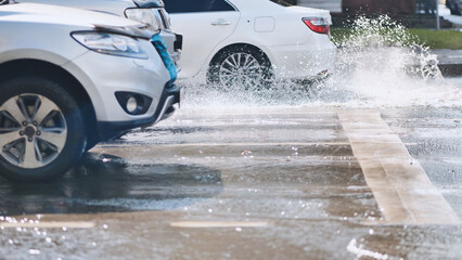 Splashing white vehicle sending water spray across urban roadway during bright daylight