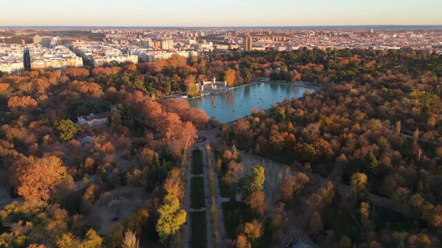 Aerial footage captures stunning view of a picturesque El Retiro park in Madrid, showcasing vibrant autumn colors, a serene lake, and diverse natural scenery that attracts visitors and nature lovers