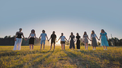 Group of high school students holding hands in a meadow at sunset, celebrating friendship and summer