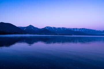 淡い青紫色の夜明けの湖と山々。