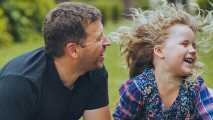 Fototapeta premium Parent and child sharing playful moment, laughing together on grassy park lawn, embodying warm family connection and joy