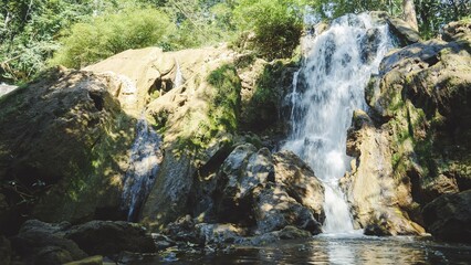 A serene waterfall cascades over moss-covered rocks, surrounded by lush greenery, in Tak Thailand.