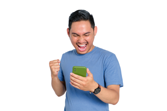 Excited young Asian man celebrating victory while looking at smartphone screen, holding phone and raising fist, isolated on transparent background