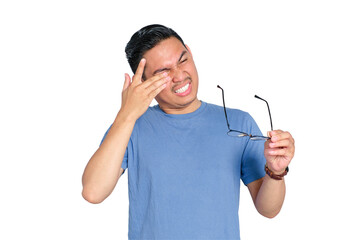 Young Asian man suffering eye discomfort while holding glasses, feeling eye strain or irritation,...