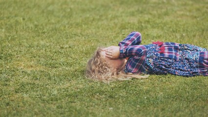 Upset child lying on verdant lawn, hands shielding face, conveying emotional isolation and...