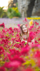 Naklejka premium A woman smiles brightly while sitting among vibrant red flowers in a picturesque garden setting.