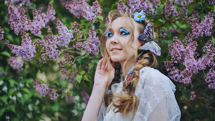 Naklejka premium Elegant model wearing colorful butterfly accessories, posing near lilac blossoms with vivid makeup, capturing springtime essence