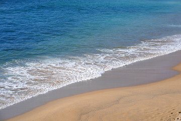 Tropical sandy beach with turquoise ocean water and gentle waves. A sunny day creates a bright, peaceful atmosphere along the shoreline, perfect for relaxation