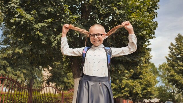 Pigtailed schoolgirl smiling, playfully twirling hair during sunny outdoor break