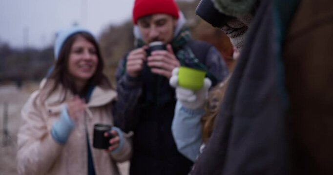 Close up a group of friends in warm clothes drink a hot drink from a cup outside the home