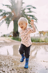 Naklejka premium Smiling little girl in rubber boots jumping on a puddle