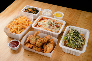 Chicken, tteokbokki, french fries, and kimbap in plastic containers
