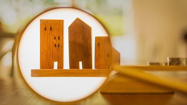 Balance with a model of a working building on the left and a pile of money on the right with a businessman's hand holding a magnifying glass.Real Estate Management Concepts.