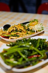 Close-up of Thai dishes of stir-fried morning glory (Kang Kong) and red curry chicken and a fresh coconut on a table with gingham tablecloth at Cliff Restaurant, Patok Bay - Ko Racha Yai, Thailand