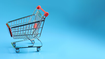 a miniature shopping cart, angled to the left, positioned against a solid blue background