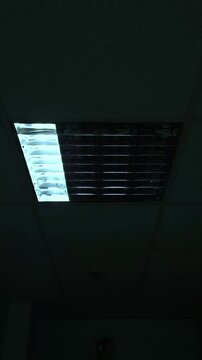 A flickering fluorescent ceiling light in a dimly lit office space. The unstable glow creates an eerie and unsettling atmosphere.
