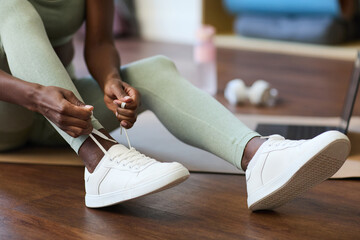 Close-up view of unrecognizable woman tying sneakers in contemporary home gym environment preparing...