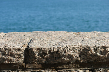 a close-up of two layers. A textured imperfect stone granite ledge with rugged surface. A serene blue hue sea at the back. 