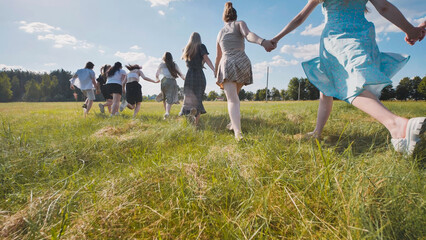 Fototapeta premium High school students holding hands and running through a field, savoring their summer vacation