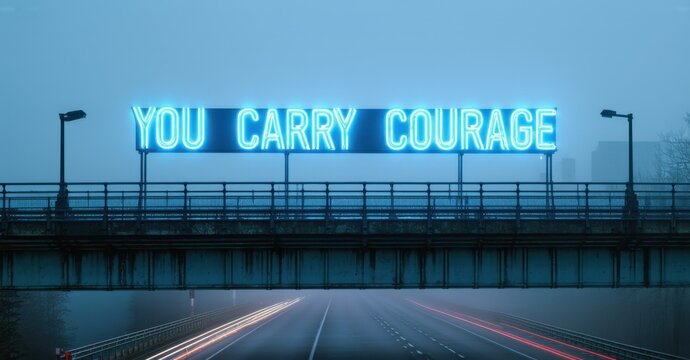 Naklejki Glowing phrase you carry courage in sky blue and white neon glowing above foggy overpass with metal railings and dim highway lights below