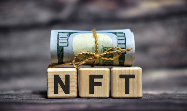 NFT - text on wooden cubes with dollars 100 bills